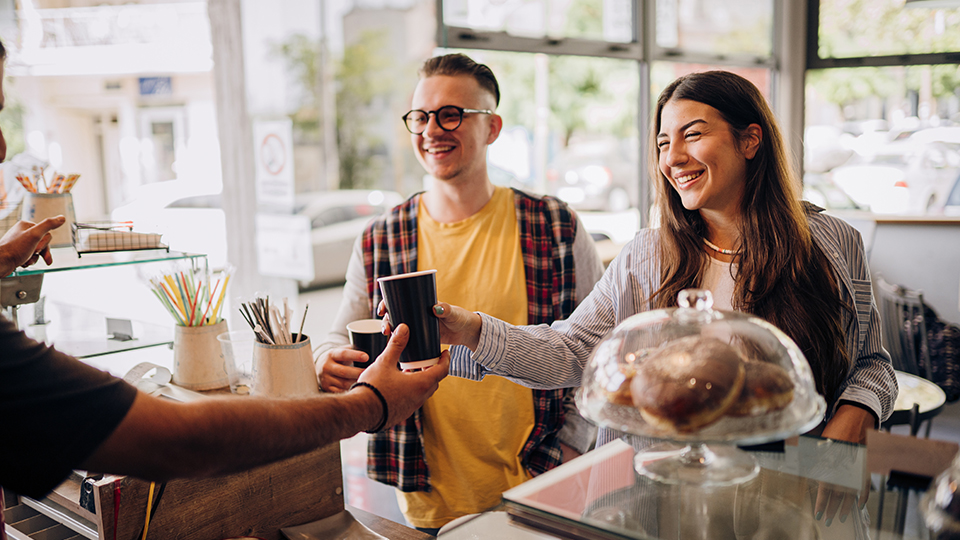 Two people at a coffee shop register, talking to barista