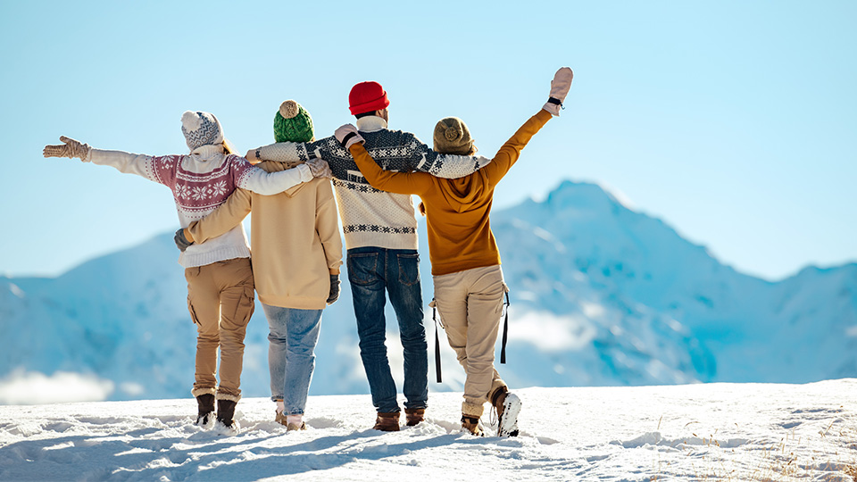 Four people in winter outfits standing on top of a snowy mountain with their arms around each other.